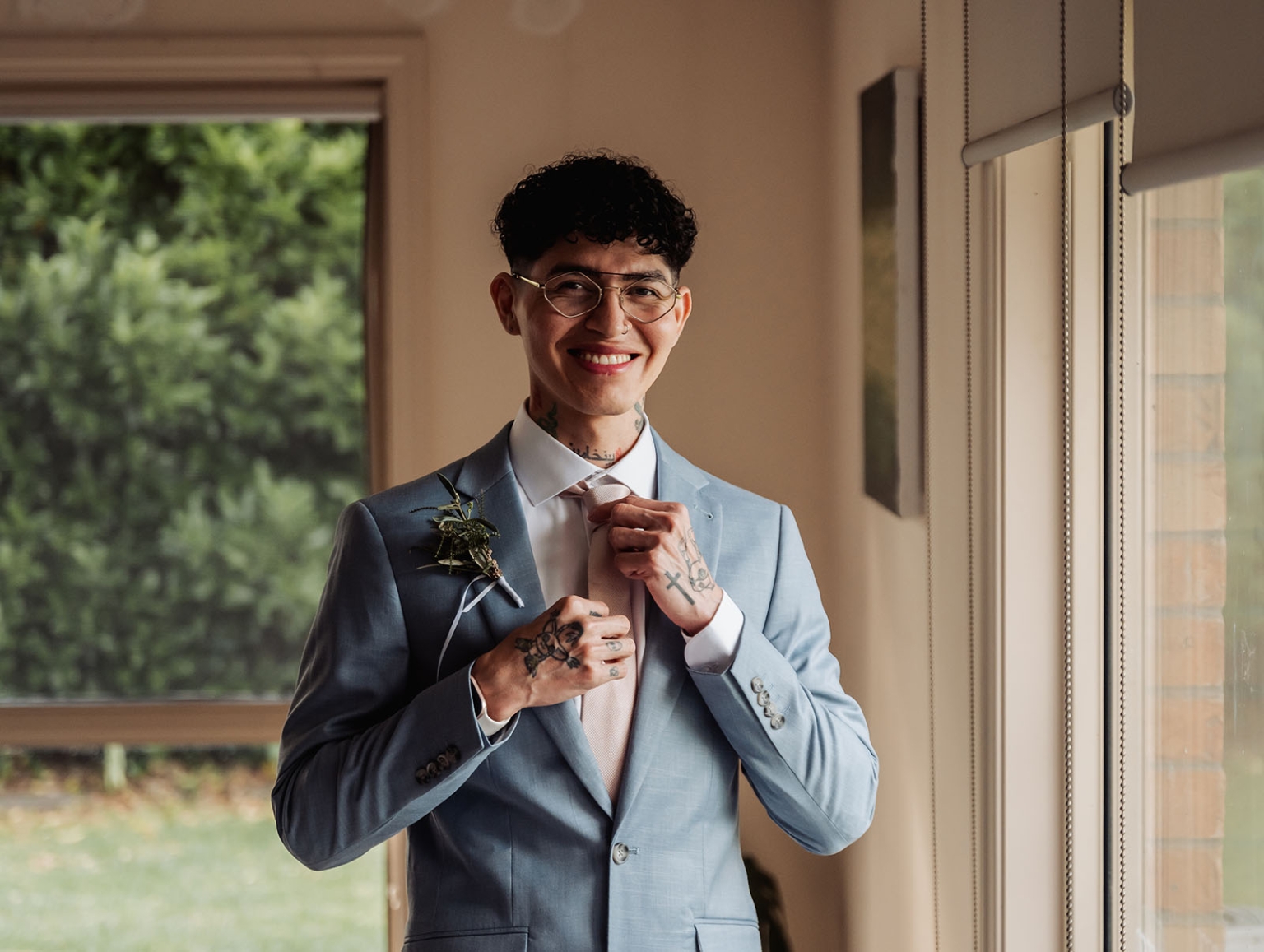 hotel royal wedding - brad & manuel 8 Smiling groom in a light blue suit adjusting his pale tie beside a window