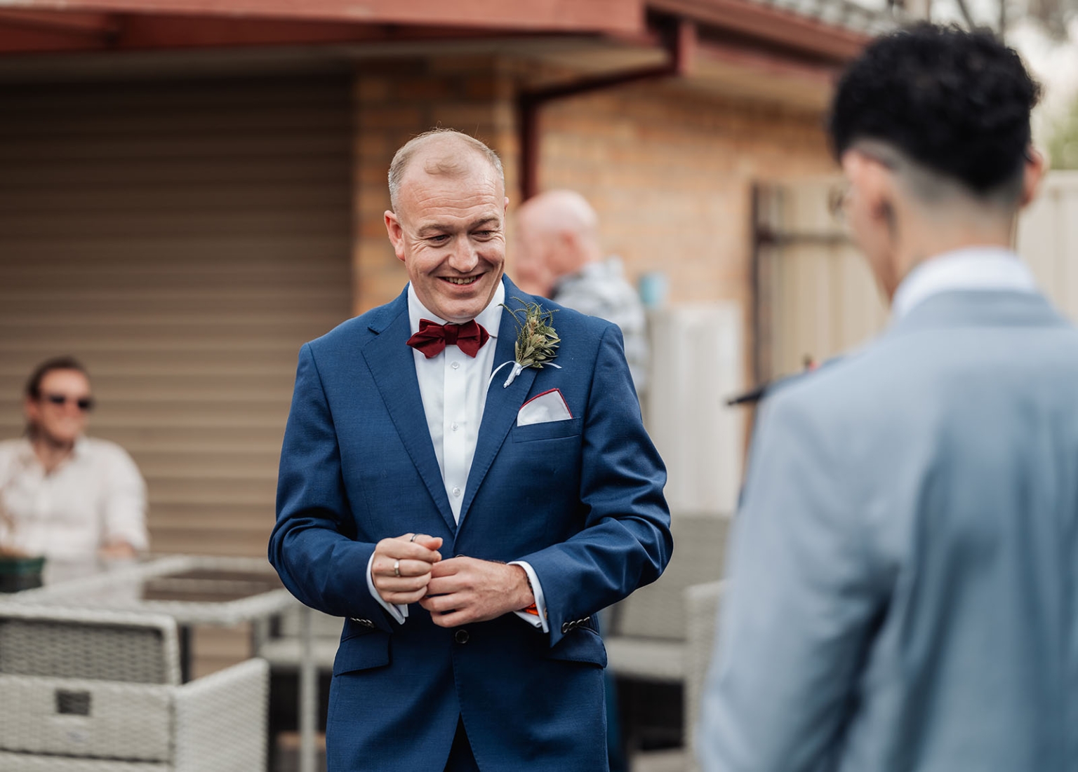 hotel royal wedding - brad & manuel 5 Smiling groom in a navy suit and burgundy bow tie facing another groom outdoors
