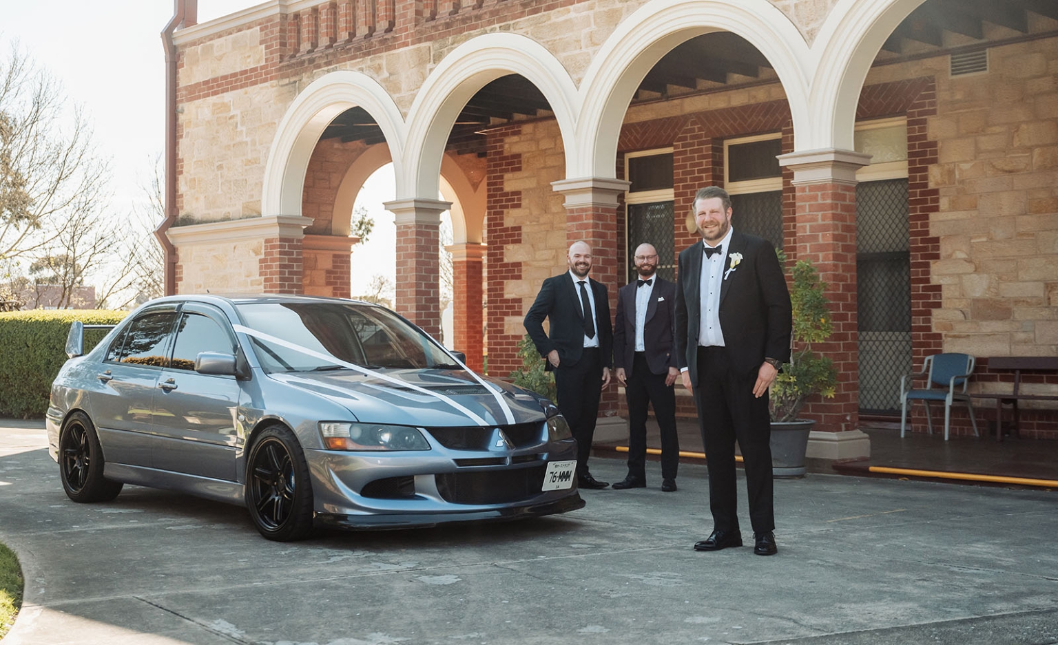 st joseph's chapel wedding – diana & michael 2 Groom and two companions in formal suits standing beside a silver car outside St Joseph's Chapel in Kensington