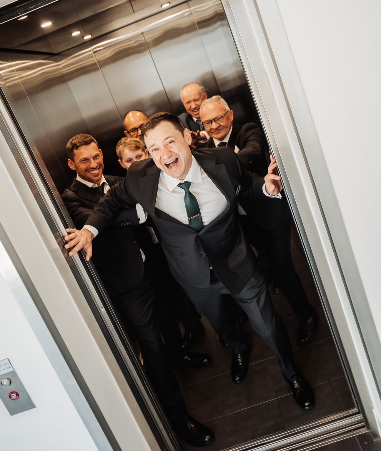 serafino winery wedding – maor & sasha 8 Groom in a green tie laughing with five groomsmen crowded into a lift before the wedding.
