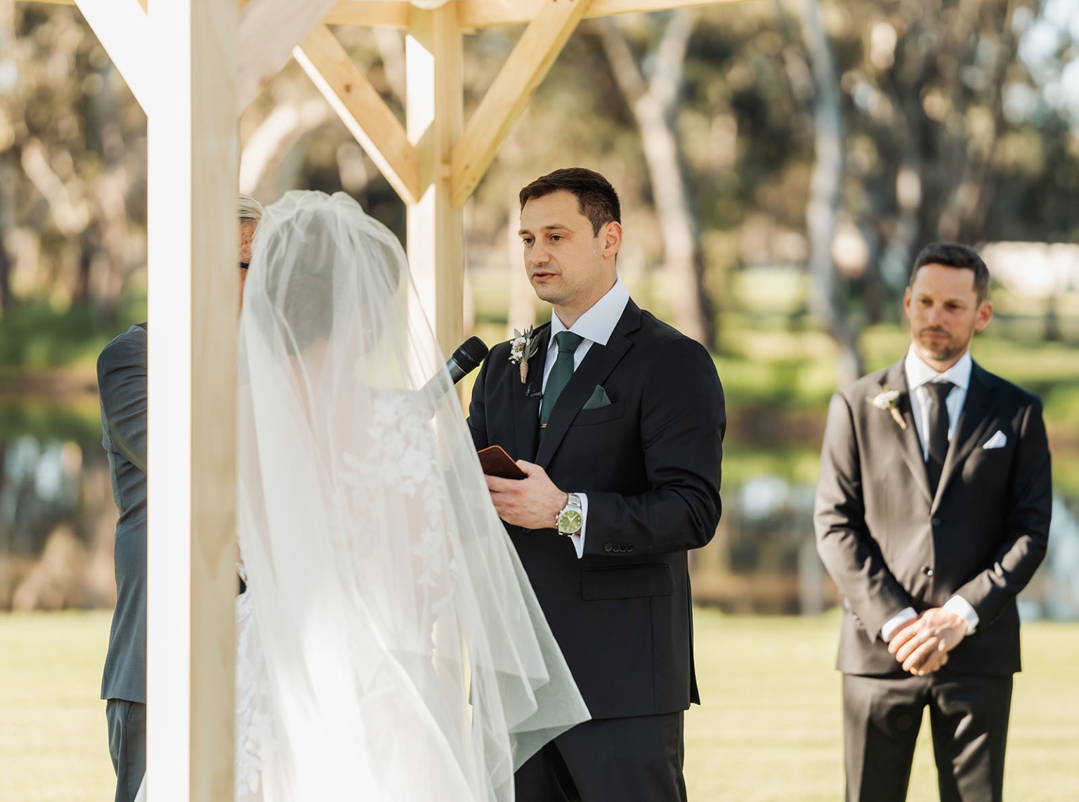 serafino winery wedding – maor & sasha 32 Groom reading vows to his veiled bride beneath a timber arbour during an outdoor wedding ceremony at Serafino Winery