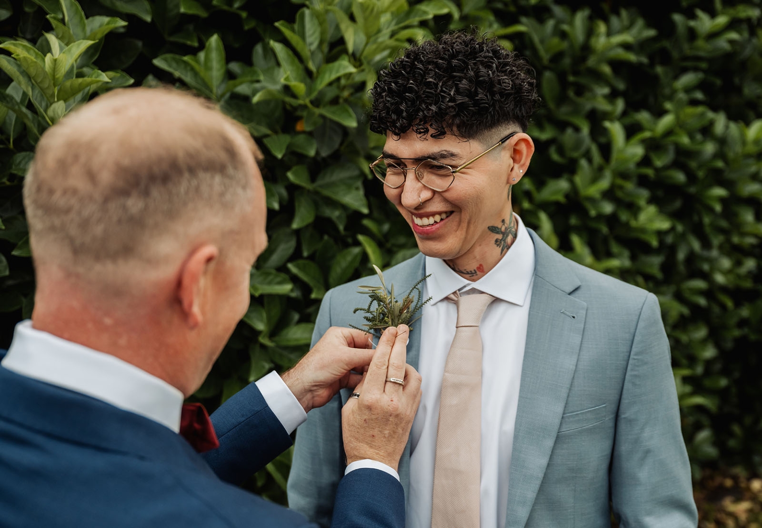 hotel royal wedding - brad & manuel 4 One groom pins a leafy buttonhole to the other groom’s light blue suit jacket as he smiles.