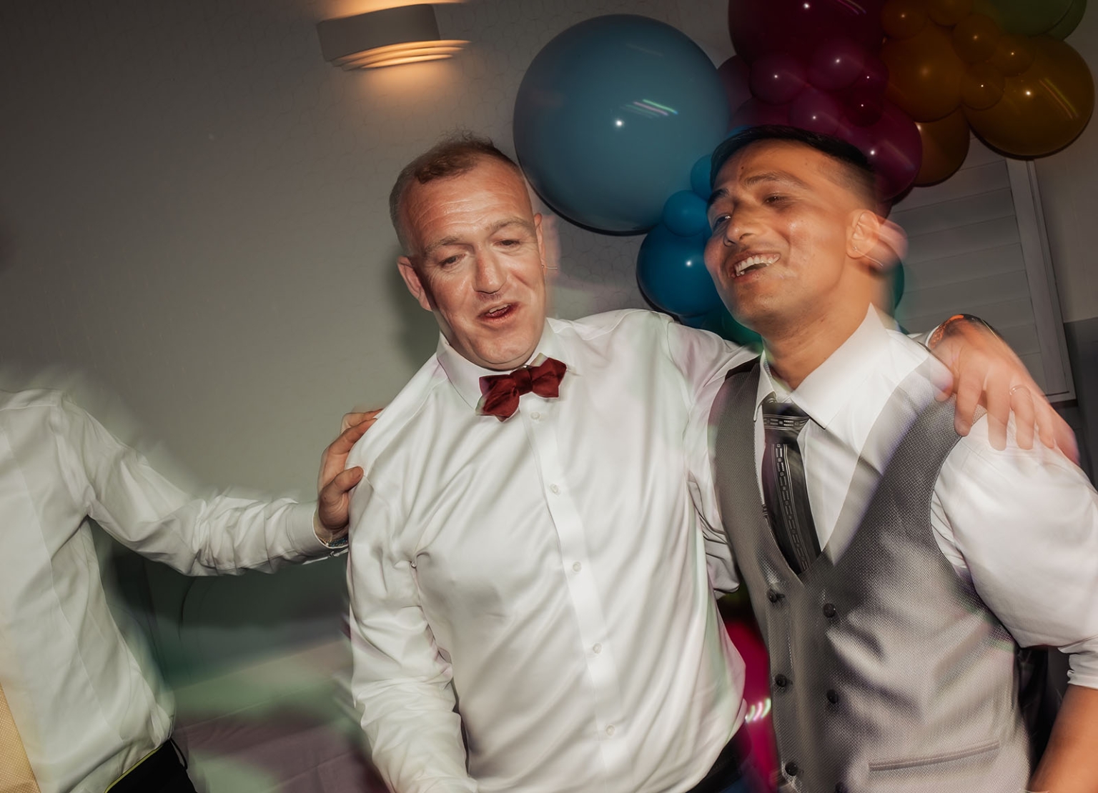 hotel royal wedding - brad & manuel 37 Two grooms dancing together in white shirts and waistcoats beneath a colourful balloon display