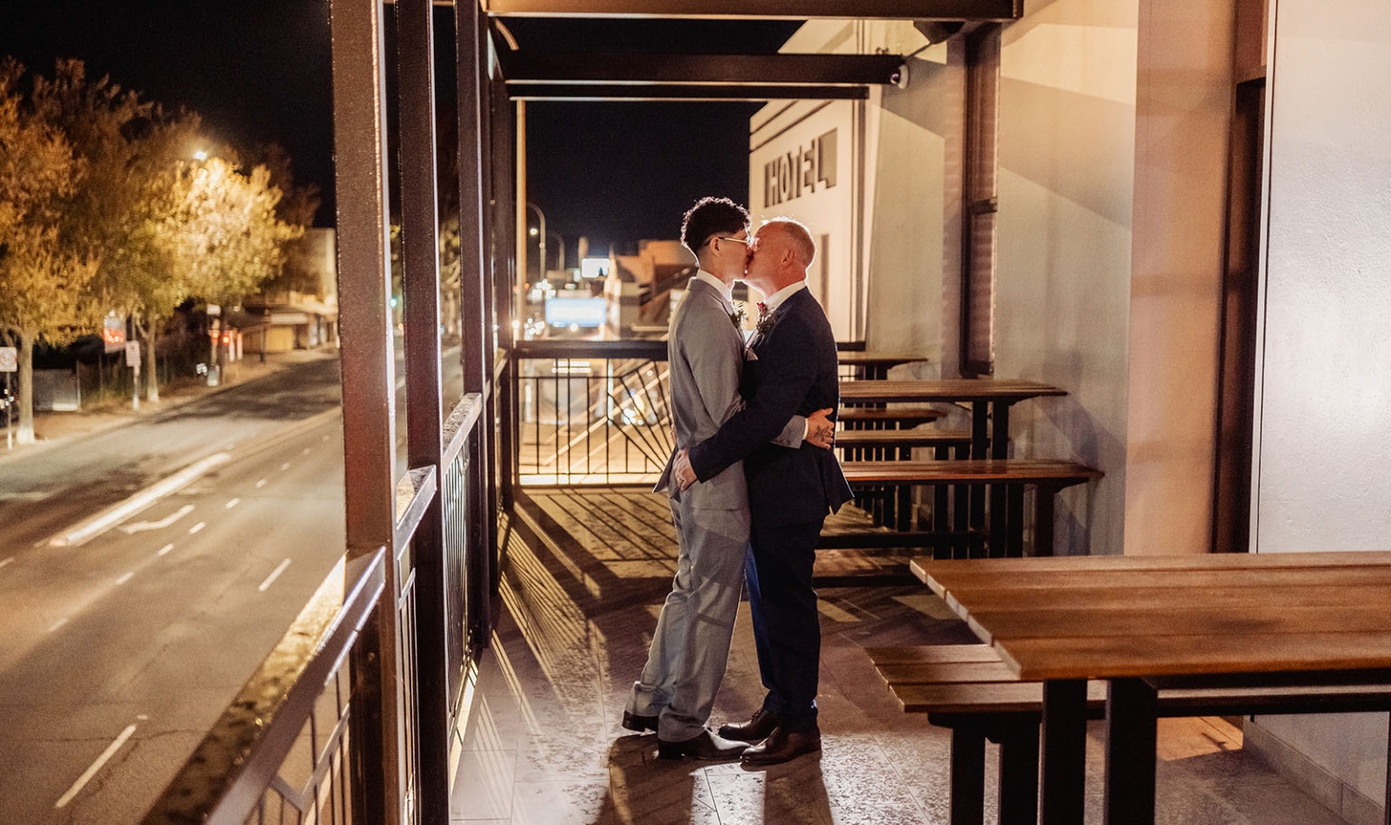 hotel royal wedding - brad & manuel 48 Two grooms in suits kissing on the outdoor balcony at Hotel Royal at night