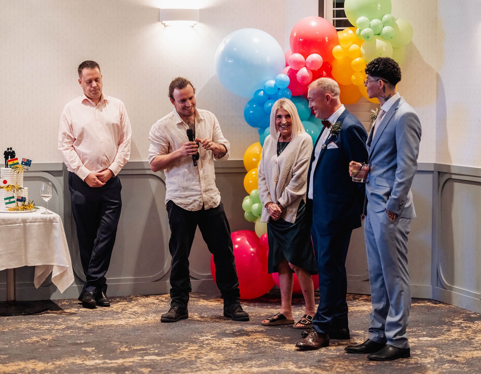 hotel royal wedding - brad & manuel 34 Wedding guest speaking beside two grooms, a decorated cake and a rainbow balloon display at Hotel Royal