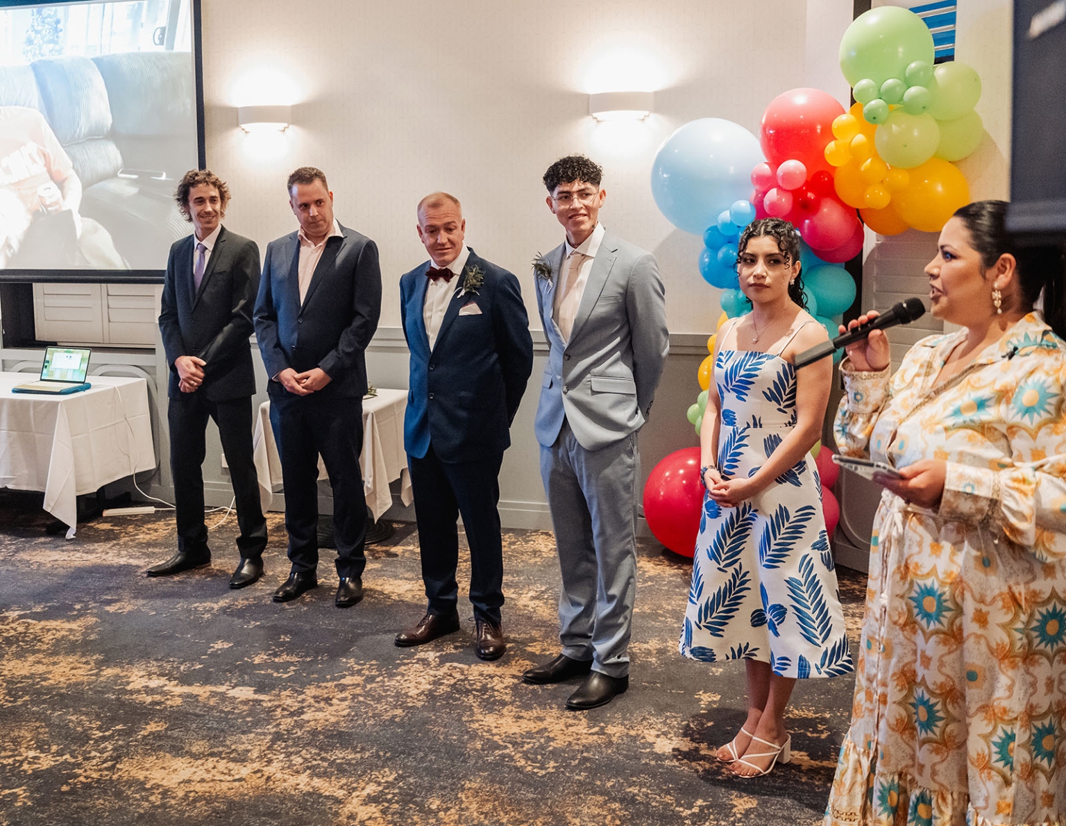 hotel royal wedding - brad & manuel 24 Wedding guests stand beside a colourful balloon display while a woman gives a speech into a microphone.