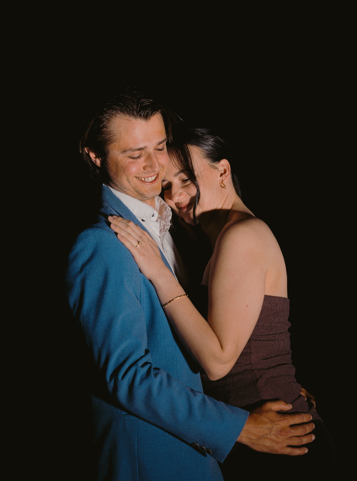 Kelly and Josh embracing and smiling at night, with her engagement ring visible on her hand