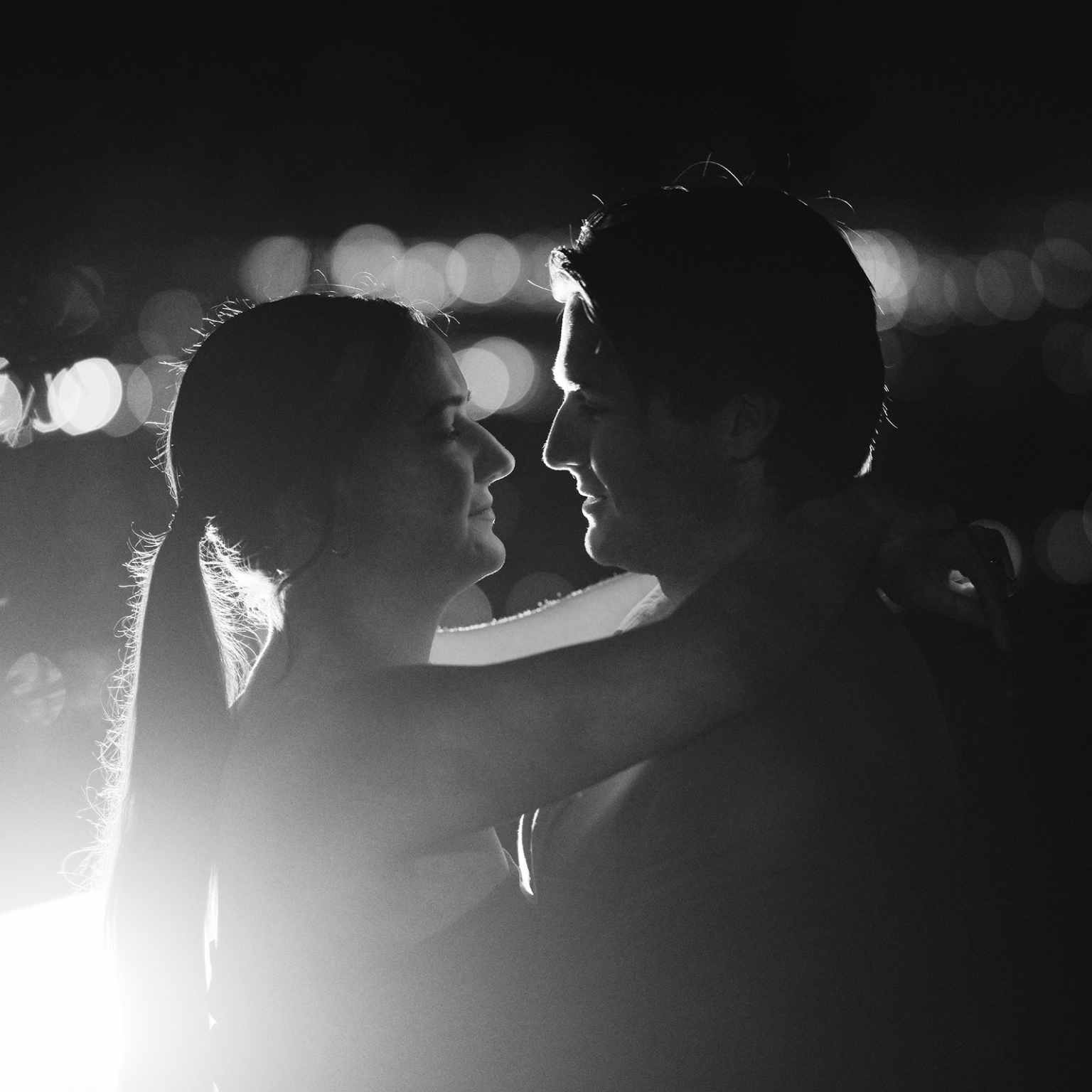 Kelly and Josh embracing at night, silhouetted against Adelaide city lights at Windy Point Lookout