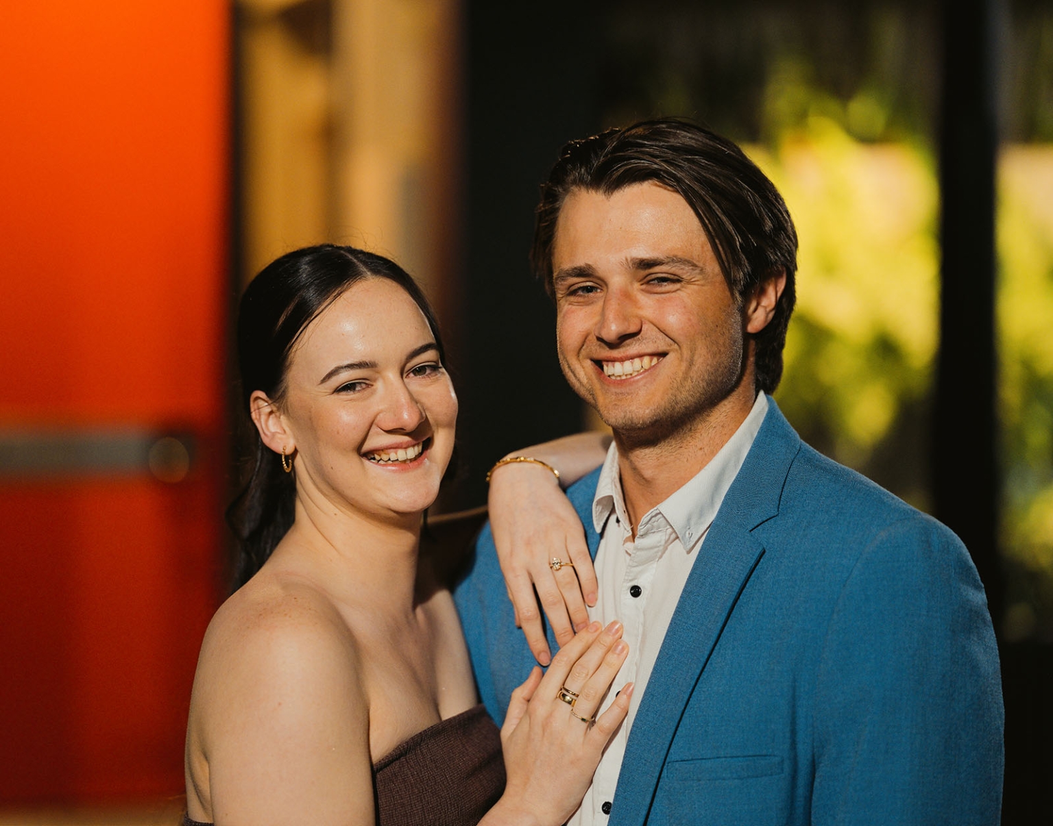 Kelly and Josh smiling together, with Kelly's engagement ring visible as she rests her hands on Josh's chest