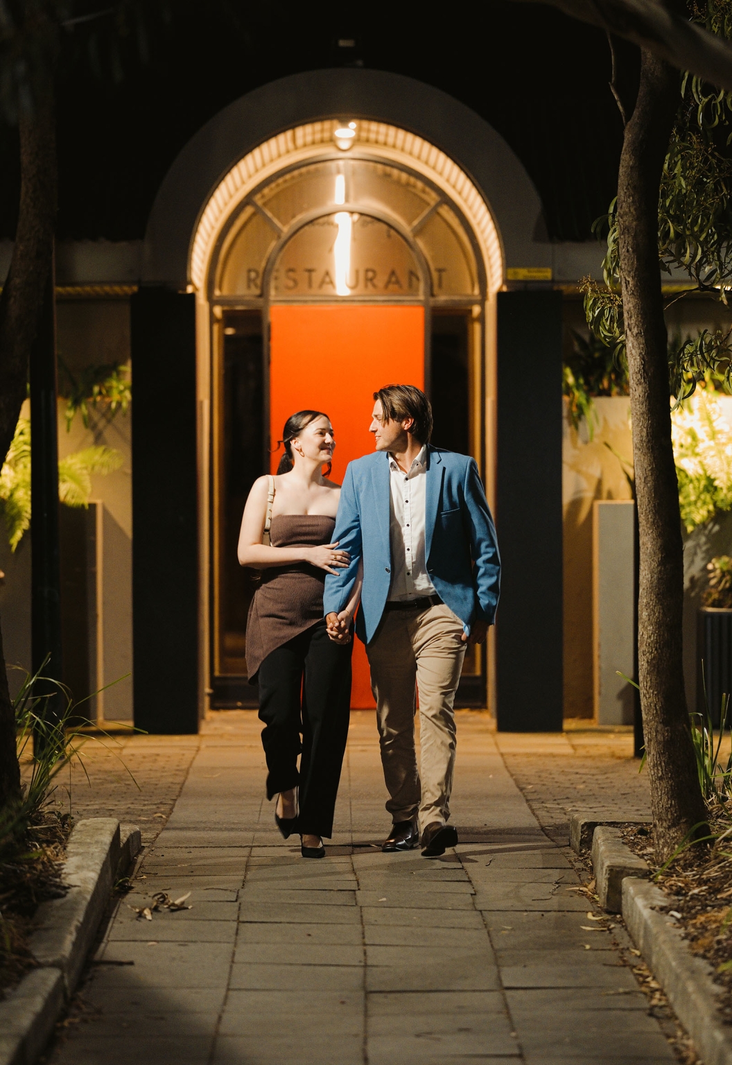 Kelly and Josh holding hands outside the illuminated entrance to Windy Point Restaurant at night
