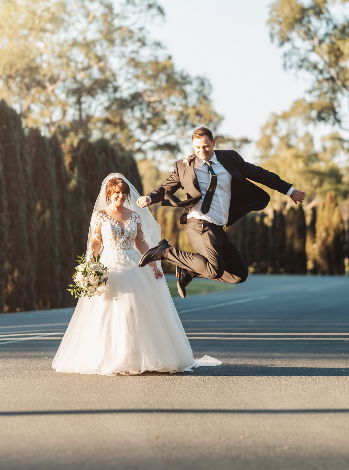 serafino winery wedding – maor & sasha 43 Groom jumping beside smiling bride in a lace wedding dress holding a bouquet at Serafino Winery