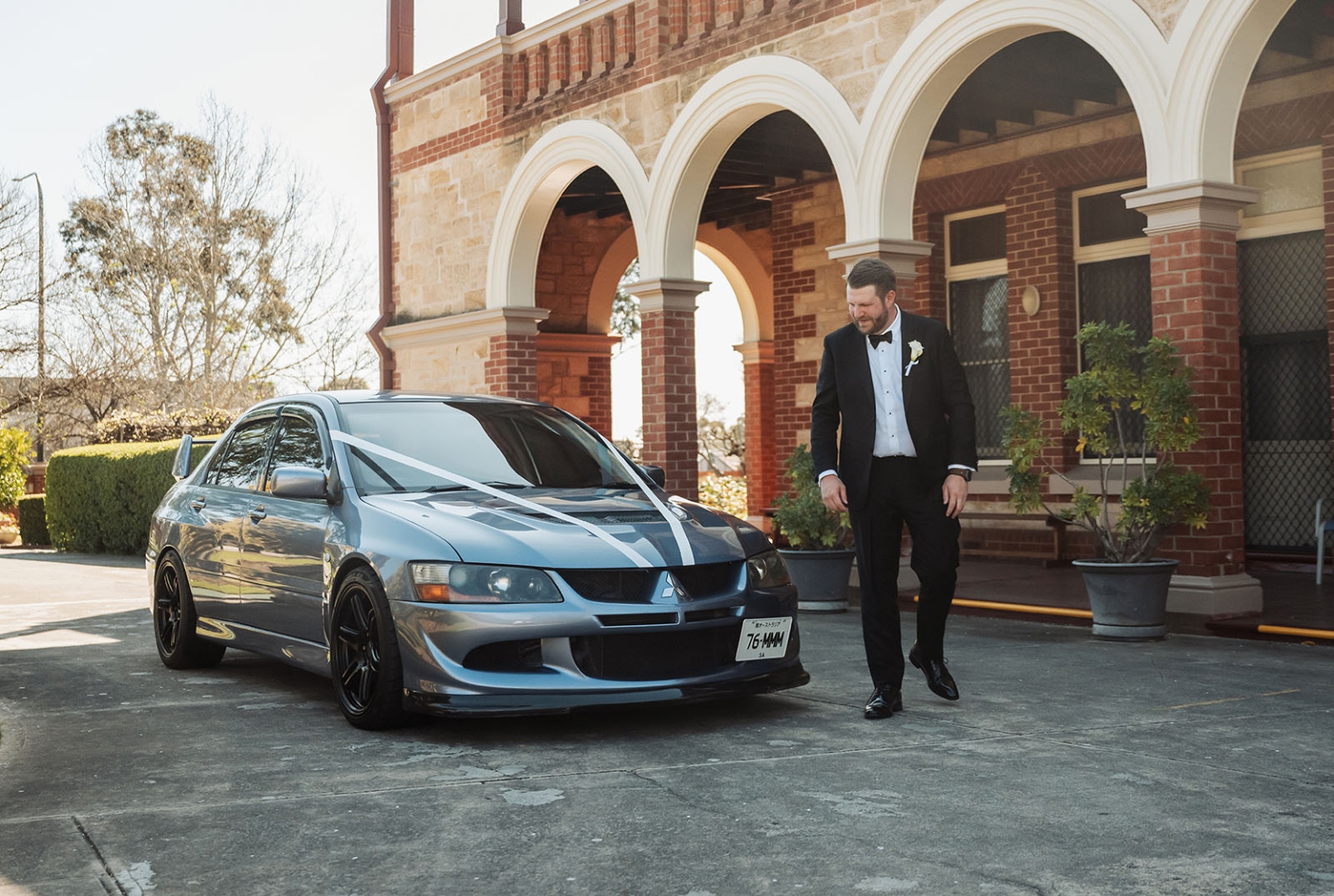 st joseph's chapel wedding – diana & michael 1 Michael in a black tuxedo walking beside a silver ribbon-decorated car outside St Joseph's Chapel