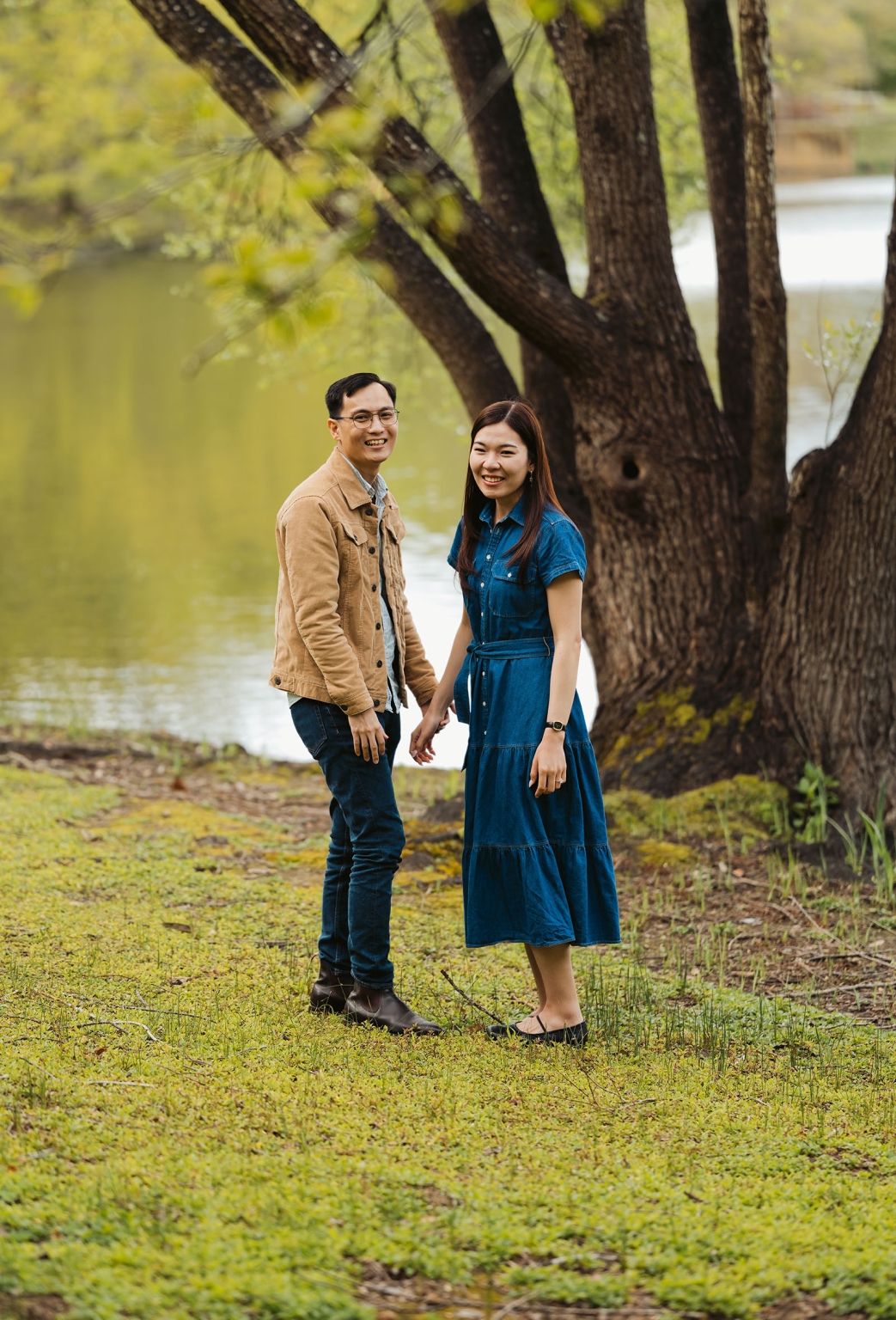 mt lofty botanic park proposal – watay & phouthun 4 Smiling couple holding hands beside a lake beneath large trees at Mount Lofty Botanic Garden