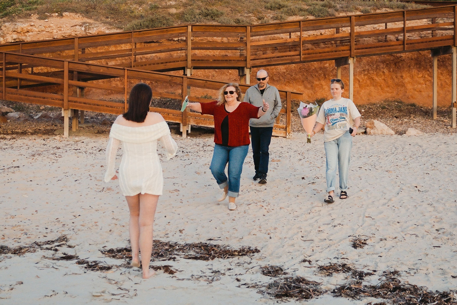 moonta's simms cove proposal – zoe & nathan 9 Woman in a white dress walking towards three people on the sand, one holding a bouquet, at Simms Cove in Moonta