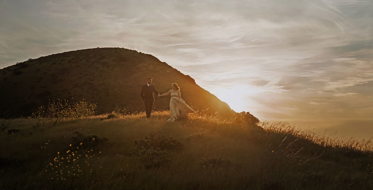 Ebony and Punit holding hands on a grassy hillside at sunset in Second Valley, South Australia