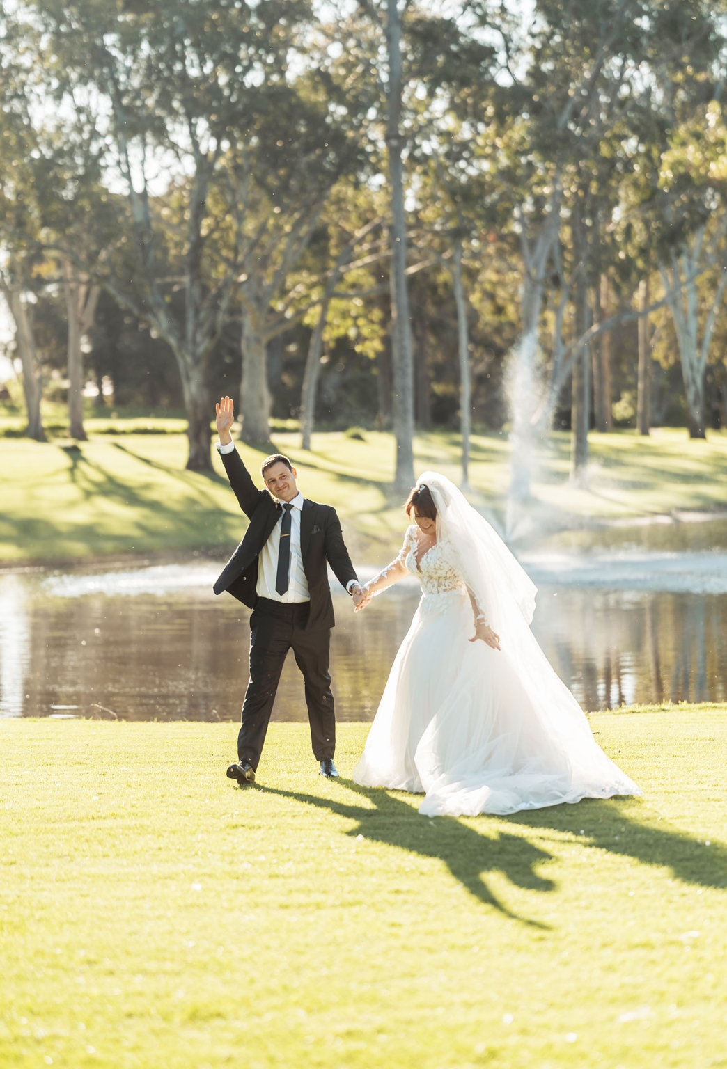 serafino winery wedding – maor & sasha 37 Bride and groom holding hands beside a lake at Serafino Winery, with the groom raising one arm