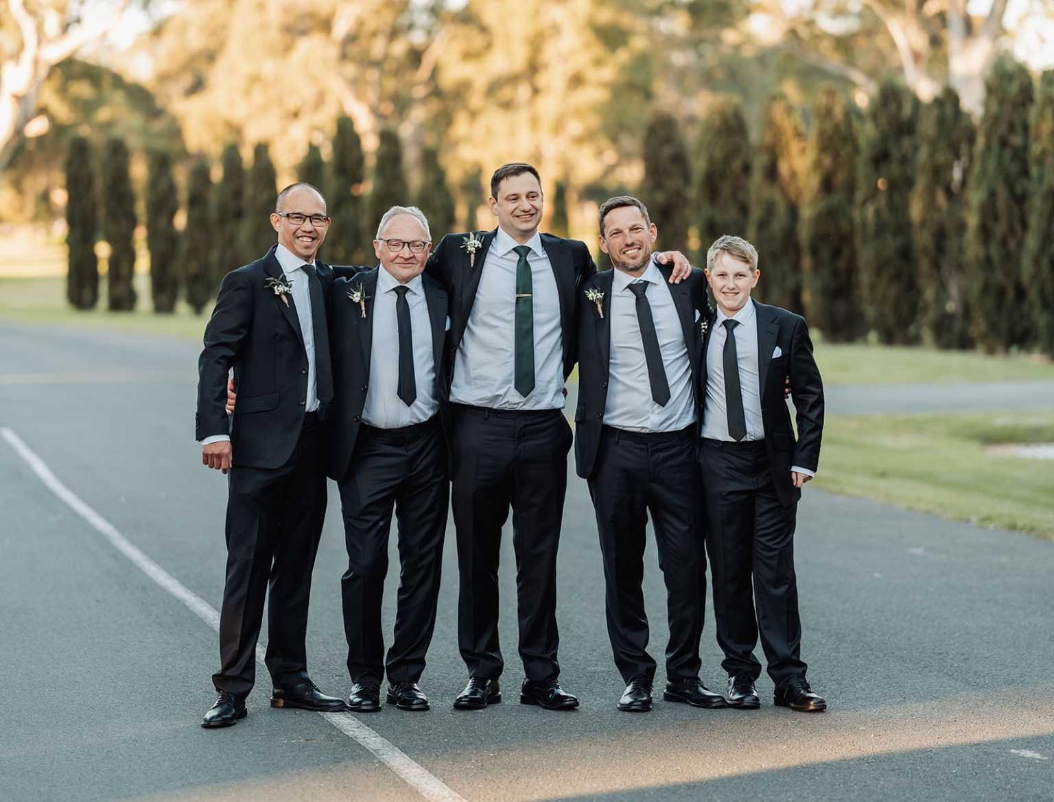 serafino winery wedding – maor & sasha 46 Groom and four groomsmen in black suits standing together on a tree-lined road at Serafino Winery