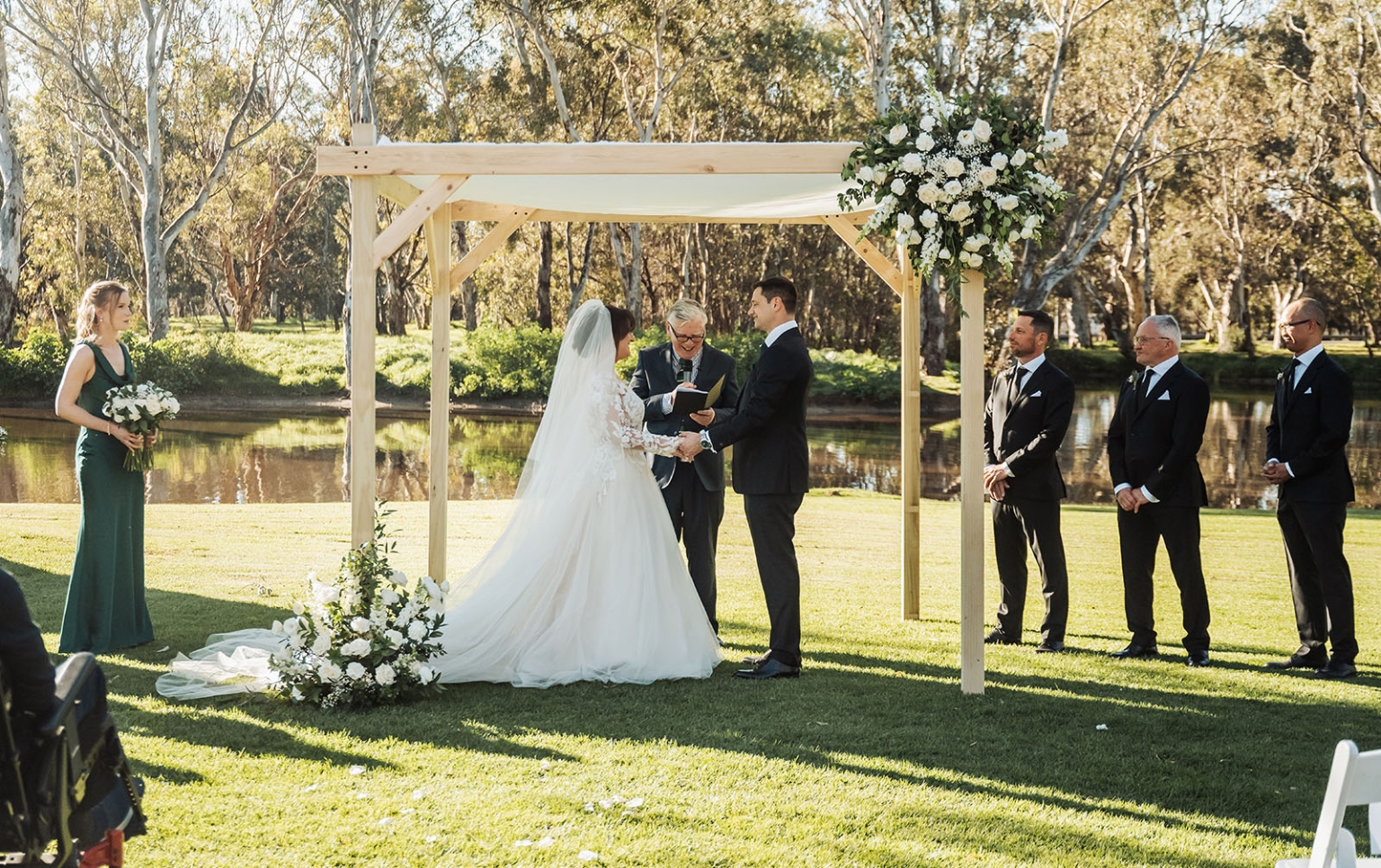 serafino winery wedding – maor & sasha 27 Bride and groom holding hands beneath a flower-decorated timber arbour during their outdoor wedding ceremony at Serafino Winery