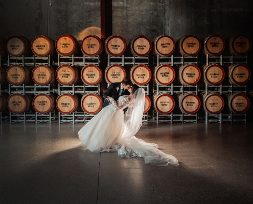 Bride and groom kissing in front of stacked Serafino Wines barrels at Serafino Winery