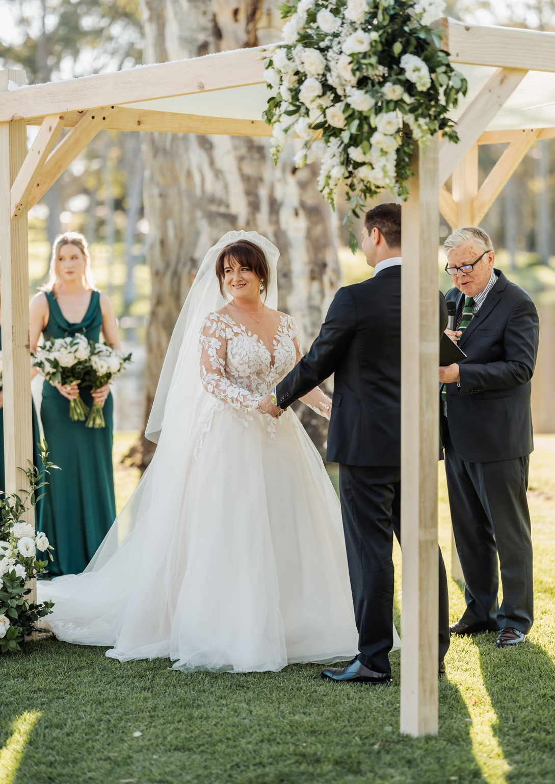 serafino winery wedding – maor & sasha 28 Bride and groom holding hands beneath a wooden arbour decorated with white flowers during their wedding ceremony at Serafino Winery.