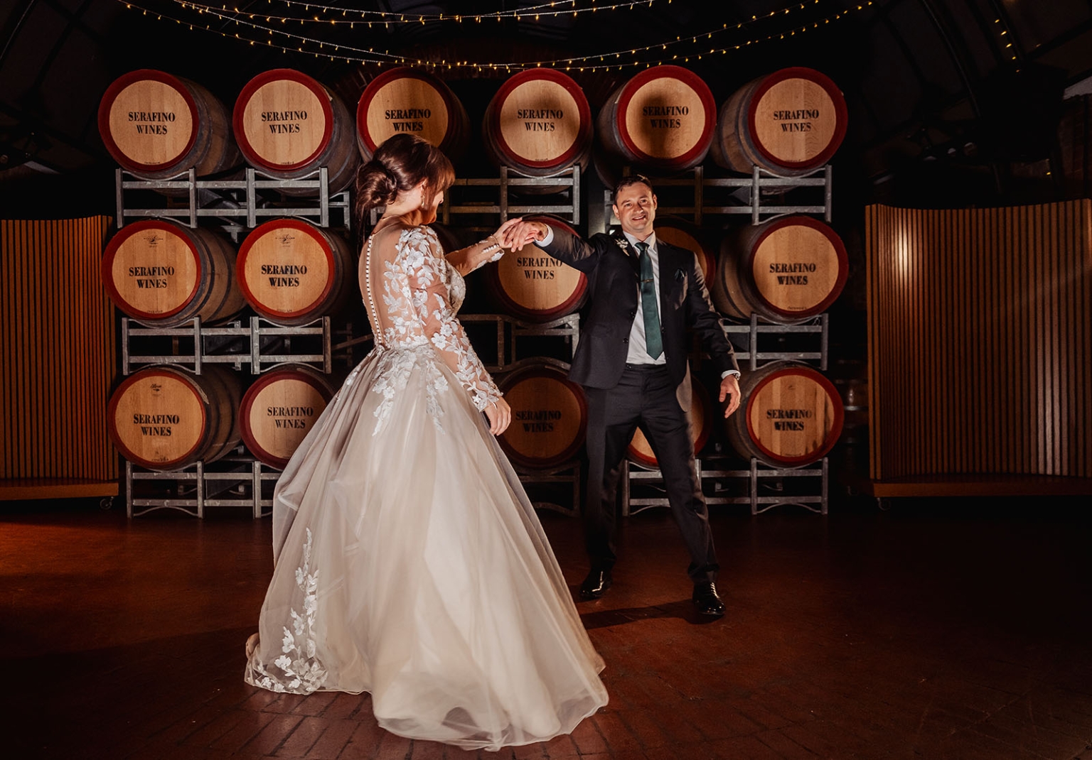 serafino winery wedding – maor & sasha 61 Bride and groom dancing beneath festoon lights in front of Serafino Wines barrels at Serafino Winery