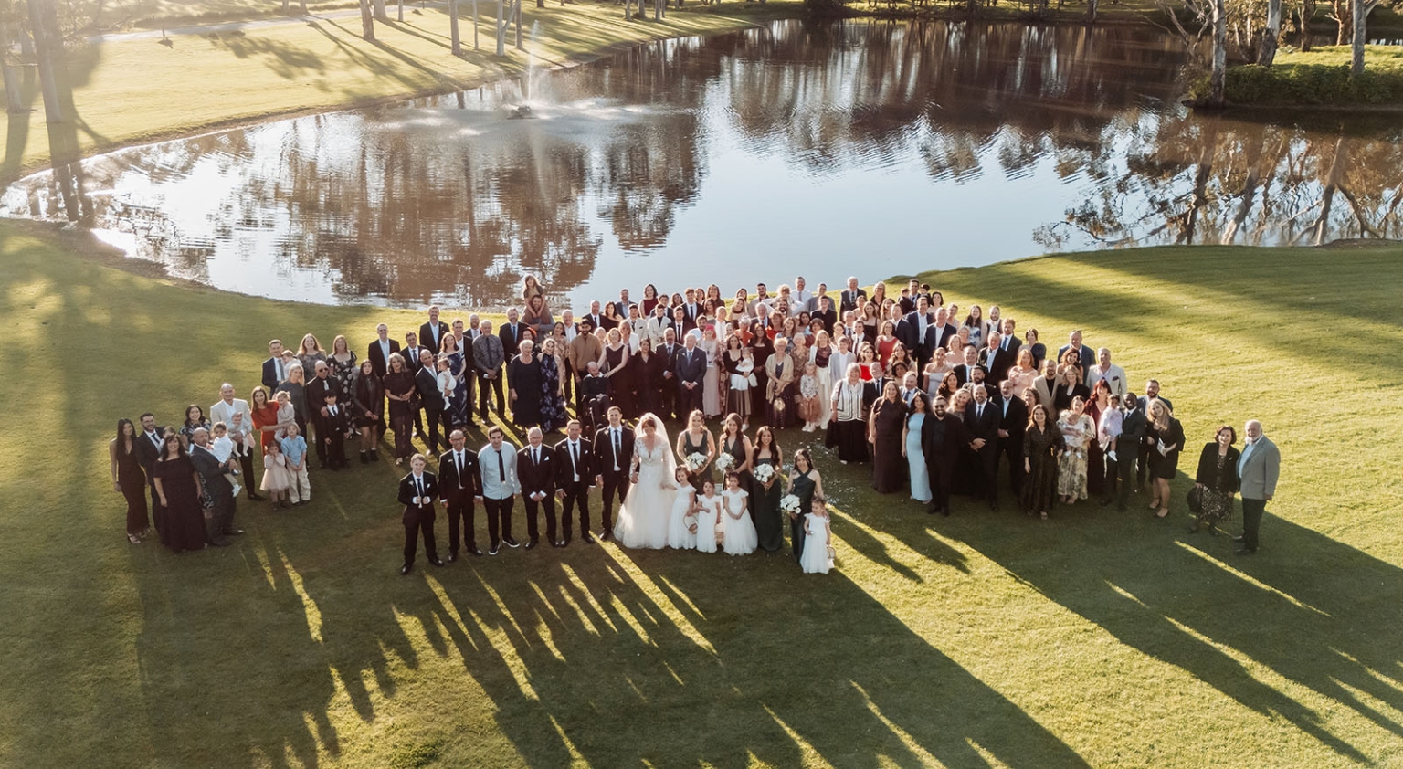 serafino winery wedding – maor & sasha 38 Aerial view of wedding guests gathered with the couple on a lawn beside a pond at Serafino Winery