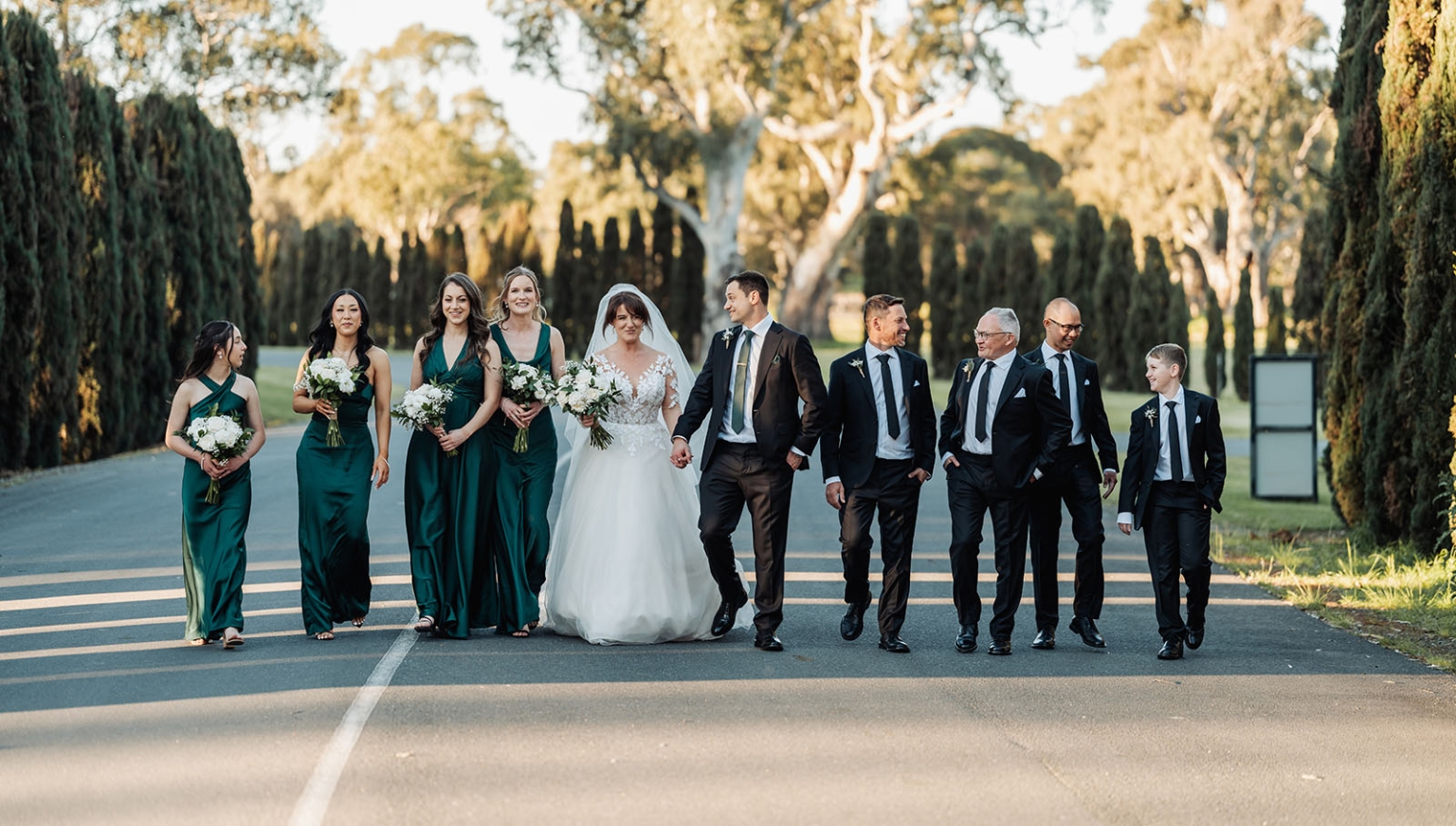 serafino winery wedding – maor & sasha 44 Bride and groom walking with their wedding party along a tree-lined driveway at Serafino Winery