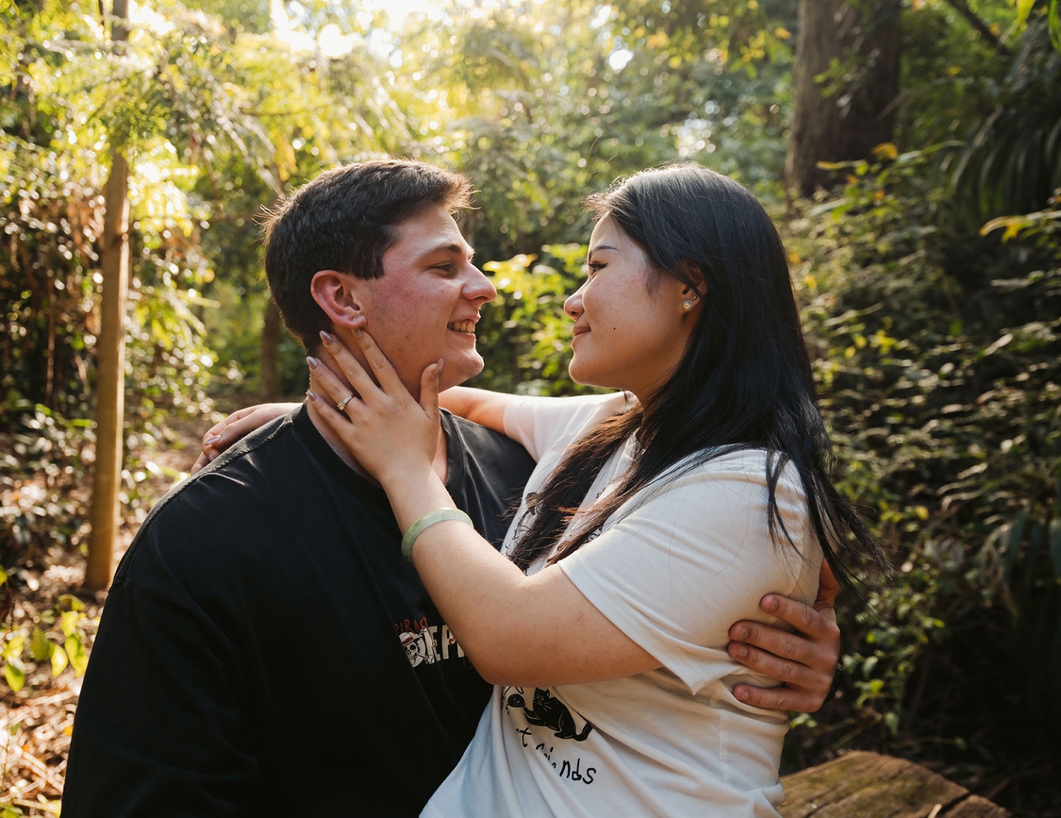 adelaide botanic gardens proposal – stewart & levi 10 Stewart and Levi embracing in a sunlit garden, with an engagement ring visible on Levi’s hand