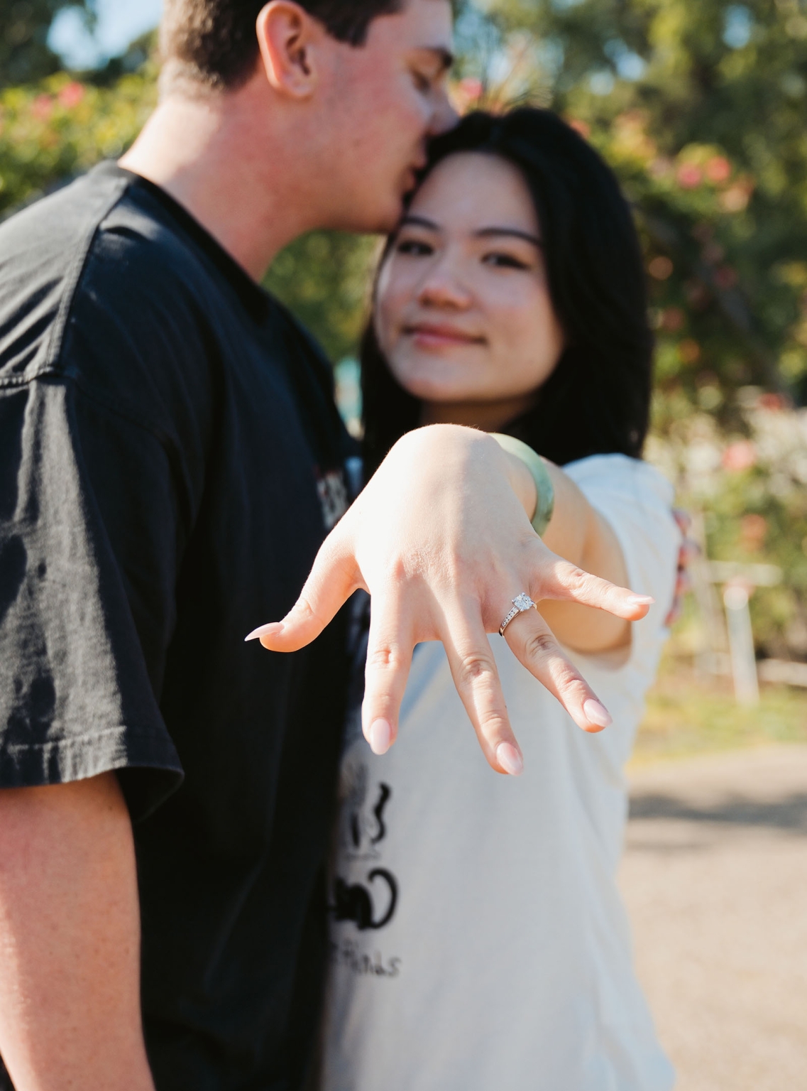 adelaide botanic gardens proposal – stewart & levi 4 Levi holds out her hand to show her engagement ring as Stewart kisses her forehead at Adelaide Botanic Gardens.