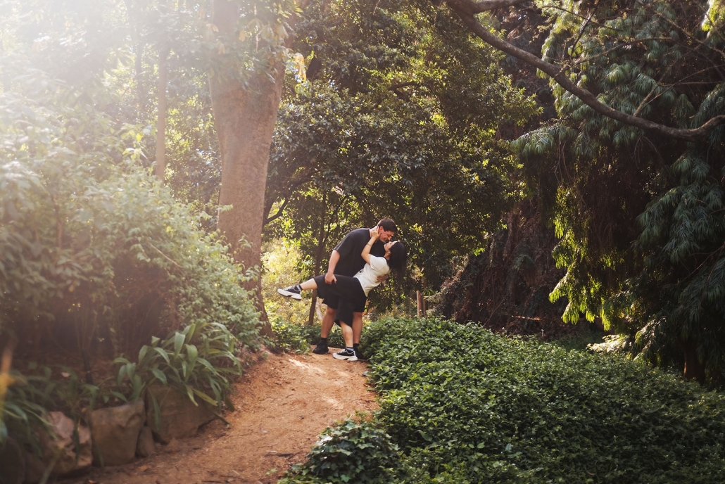 adelaide botanic gardens proposal – stewart & levi 29 Stewart lifts Levi in an embrace on a sunlit path surrounded by dense greenery at Adelaide Botanic Gardens.