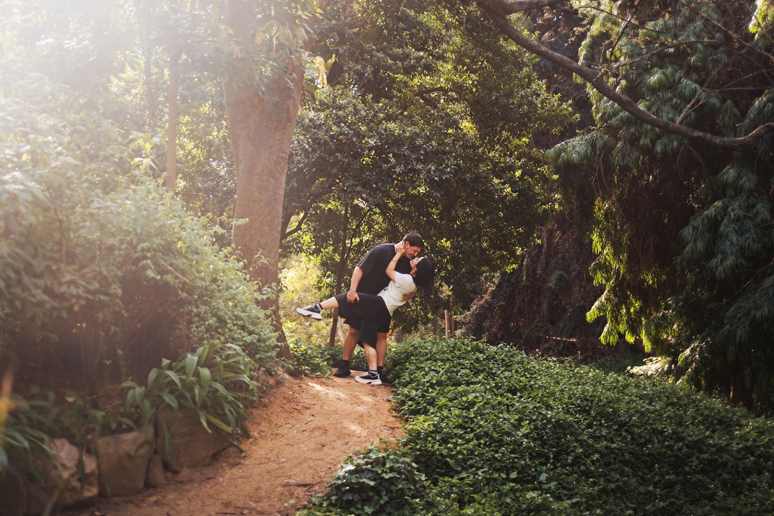 adelaide botanic gardens proposal – stewart & levi 11 Stewart lifts Levi in an embrace on a sunlit path surrounded by dense greenery at Adelaide Botanic Gardens.