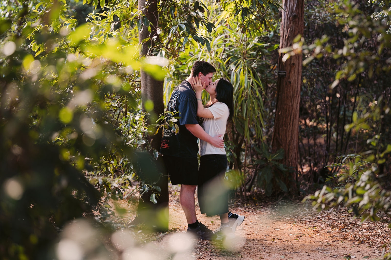 adelaide botanic gardens proposal – stewart & levi 9 Stewart and Levi kissing on a leafy path at Adelaide Botanic Gardens