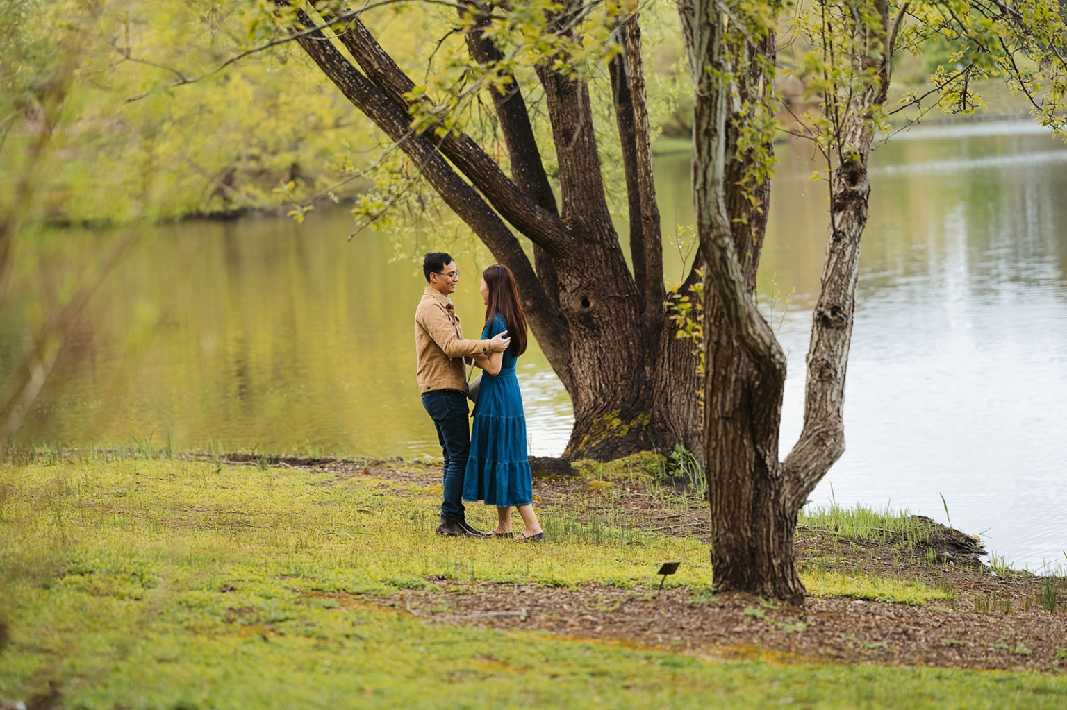 mt lofty botanic park proposal – watay & phouthun 3 Watay and Phouthun standing together beneath a large tree beside the lake at Mount Lofty Botanic Garden