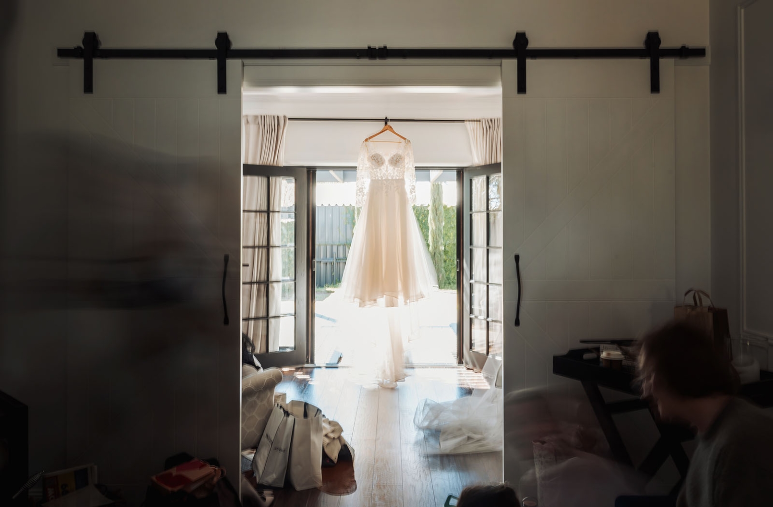 serafino winery wedding – maor & sasha 14 Lace wedding dress hanging in a bright doorway between open French doors during bridal preparations
