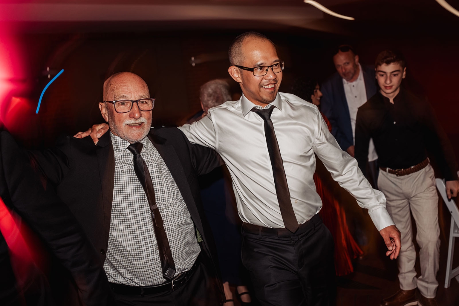serafino winery wedding – maor & sasha 67 Two male wedding guests smiling and dancing together under red party lights at Serafino Winery