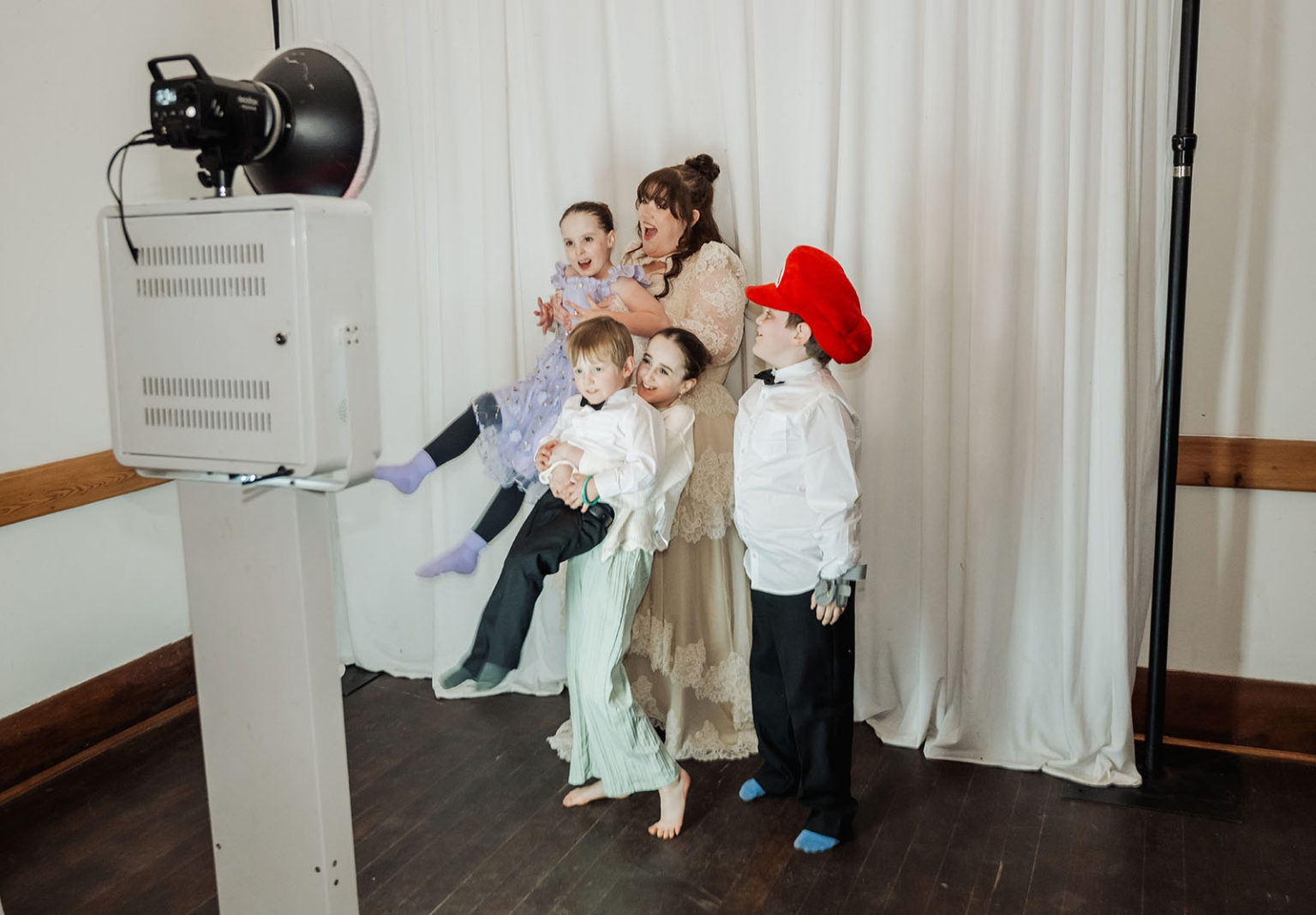 burbrook wedding – amber & angus | kuitpo forest wedding 59 Wedding guests, including three children, pose together beside a photo booth screen and studio light.