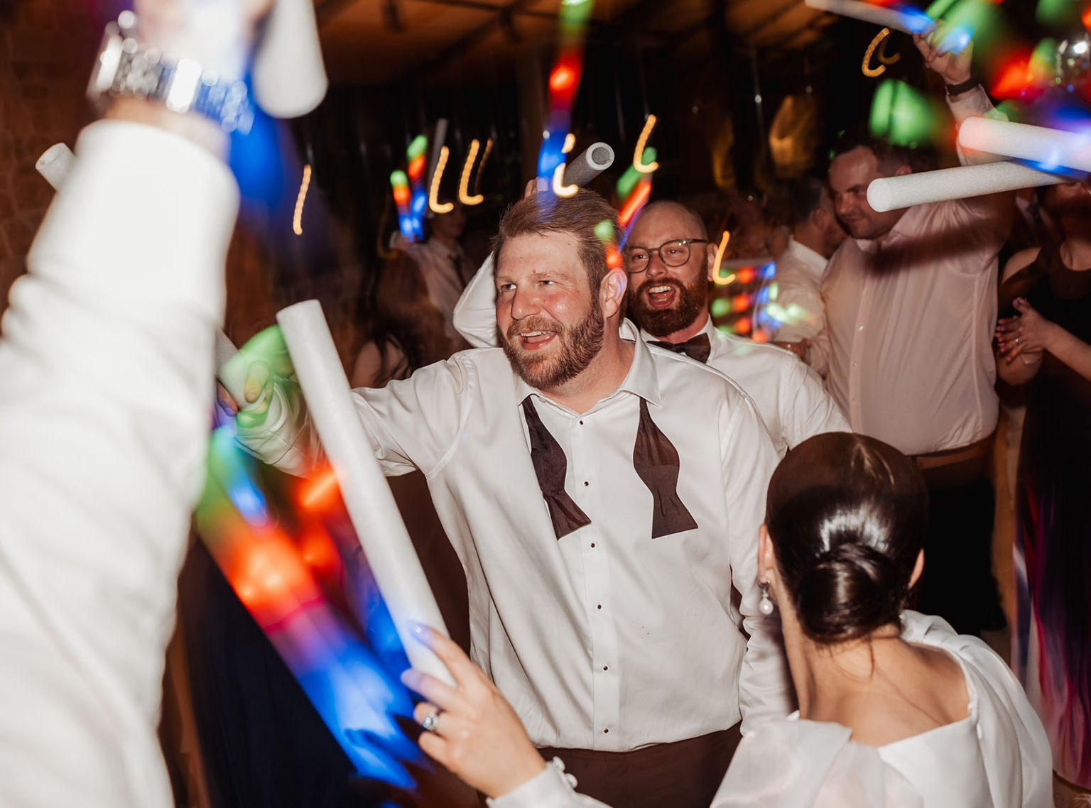 st joseph's chapel wedding – diana & michael 61 Wedding guests dancing with glowing LED foam batons at the reception, with colourful lights streaking across the scene.