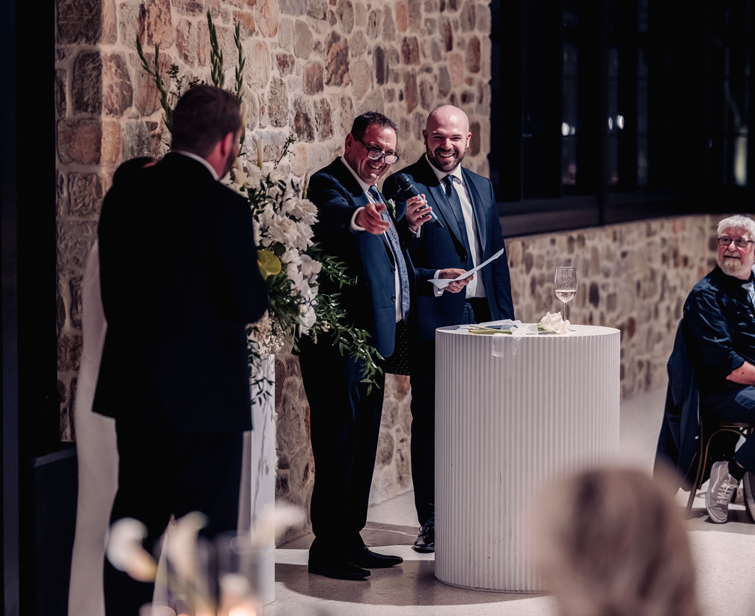 st joseph's chapel wedding – diana & michael 49 Man giving a wedding reception speech with a microphone and notes beside a floral arrangement at Sunnybrae