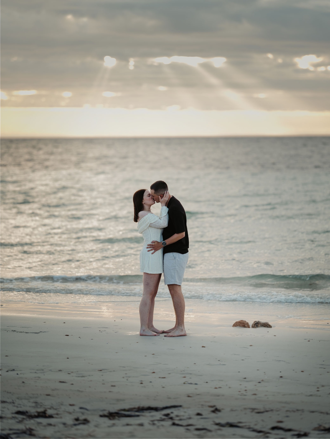 moonta's simms cove proposal – zoe & nathan 19 Zoe and Nathan kissing barefoot on the sand at Simms Cove, with gentle waves and a cloudy sunset behind them