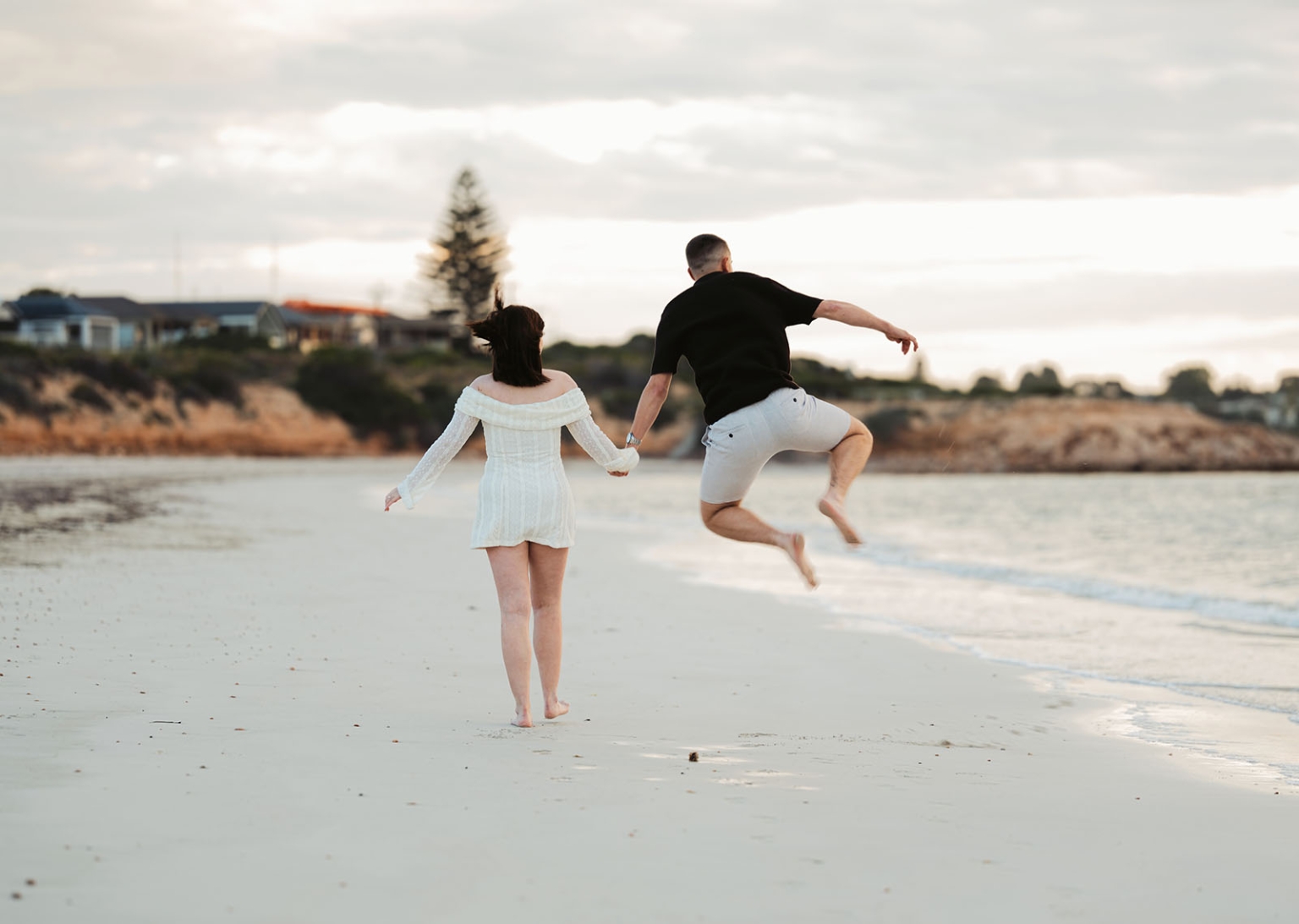 moonta's simms cove proposal – zoe & nathan 17 Zoe and Nathan holding hands as Nathan jumps on the sand at Simms Cove beach, Moonta