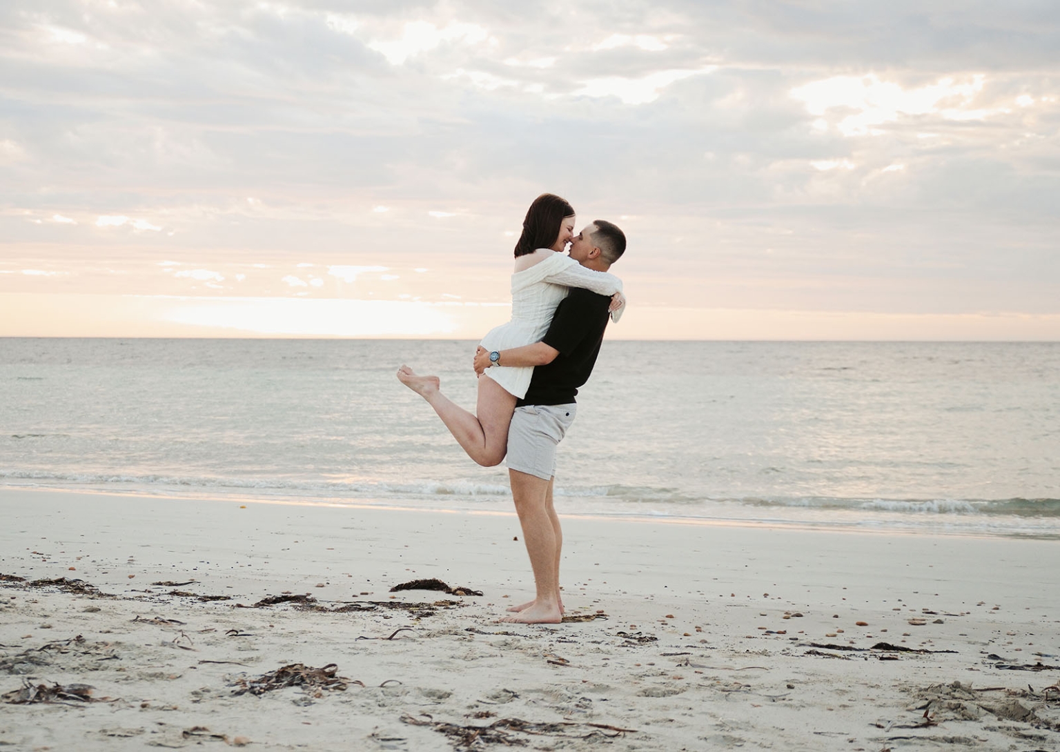 moonta's simms cove proposal – zoe & nathan 25 Zoe and Nathan embracing on Simms Cove beach at sunset, with Nathan lifting Zoe above the sand