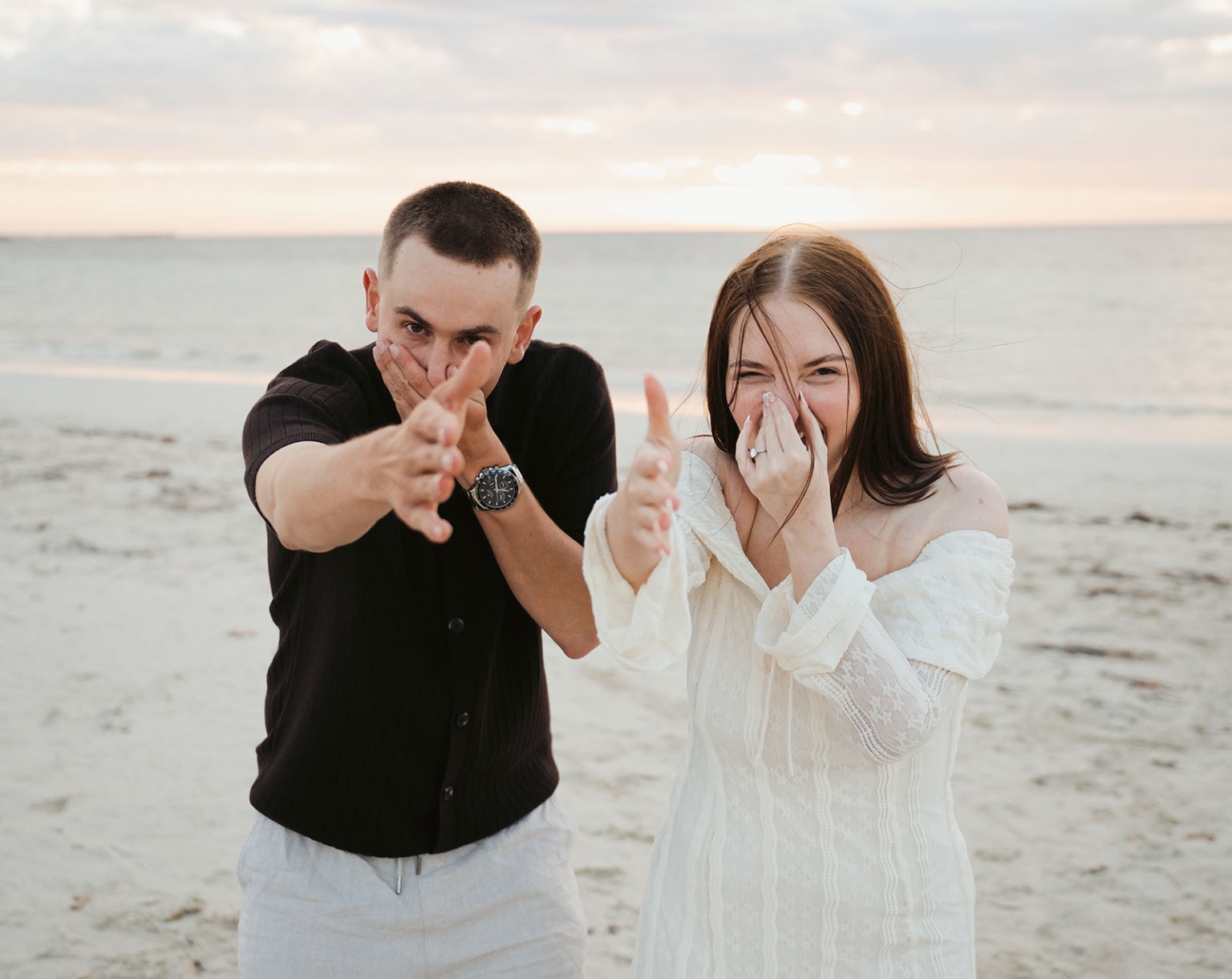 moonta's simms cove proposal – zoe & nathan 28 Zoe and Nathan laughing on Simms Cove beach, with Zoe’s engagement ring visible as they reach towards the camera