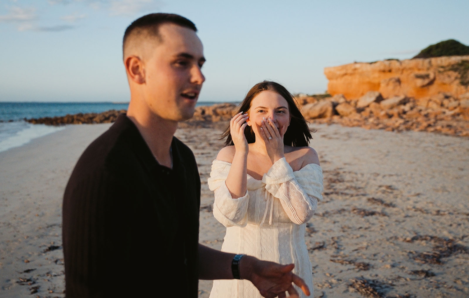moonta's simms cove proposal – zoe & nathan 5 Zoe reacts with surprise and shows her engagement ring while Nathan stands beside her on Simms Cove beach in Moonta.